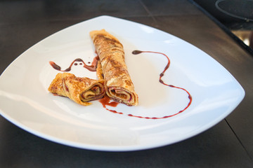 Gefüllter Crepe Pfannkuchen eingerollt und dekoriert auf weißem Teller