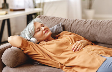 Senior woman listening to music lying on sofa