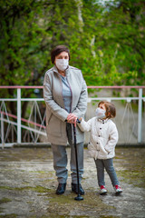 Fototapeta premium a girl and her grandmother, wearing medical masks, walk on a deserted street during the COVID-19 pandemic