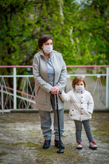 a girl and her grandmother, wearing medical masks, walk on a deserted street during the COVID-19 pandemic