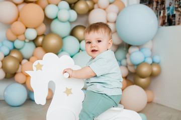 Fototapeta na wymiar Infant child baby boy kid toddler sitting ride white little wooden horse toy. Photo zone of balloons.