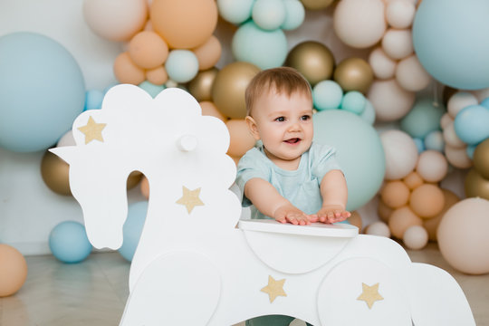 Infant child baby boy kid toddler sitting ride white little wooden horse toy. Photo zone of balloons.