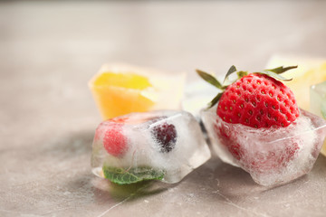 Ice cubes with different berries and mint on grey table, closeup