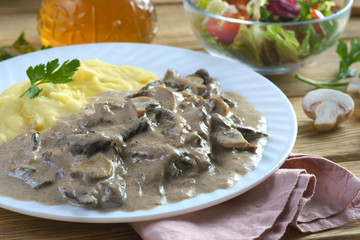 beef Stroganoff with mashed potatoes on a wooden background with mushrooms and vegetable salad