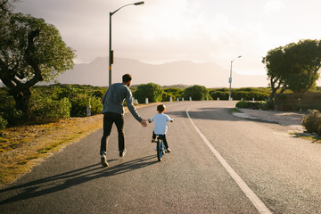 Rear view of father teaching his son to ride bicycle