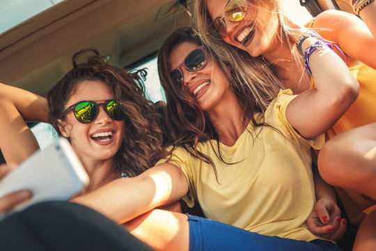 Three female friends enjoying traveling in the car. Sitting in rear seat and and making selfie.