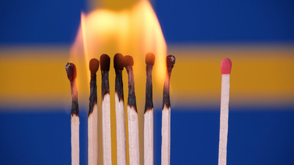 Coronavirus outbreak, social distancing concept. Burning matches on Swedish flag background. Concept: stop spreading virus, domino effect, COVID-19 pandemic, pray for Sweden