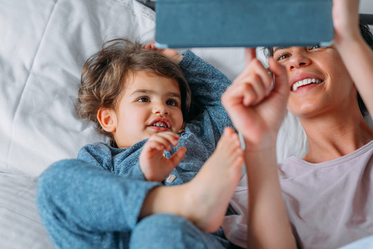 Mother and daughter watching cartoon on digital tablet while lying on bed