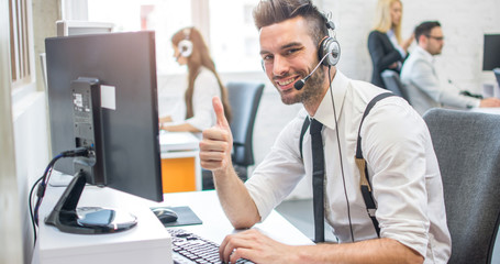 Friendly online customer support agent with headset showing thumb up in call center