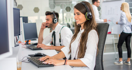Friendly smiling woman call center operator with headset using computer at office - obrazy, fototapety, plakaty