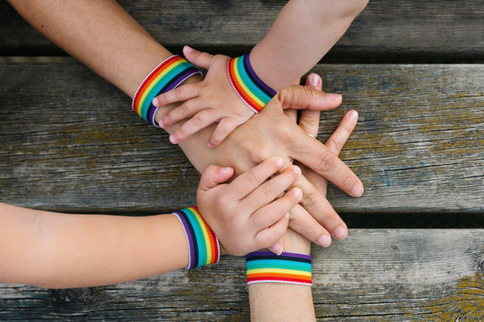 Unrecognizable persons holding hands with gay flag bracelets over wooden table