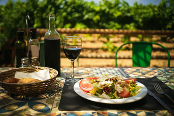 Mediterranean lunch in a farm restaurant, a glass, a bottle of wine and salad on a vineyard background