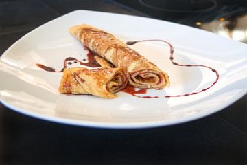 Gefüllter Crepe Pfannkuchen eingerollt und dekoriert auf weißem Teller