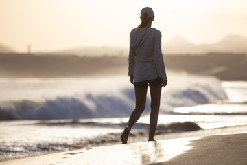 Young woman walking along ocean beach with waves