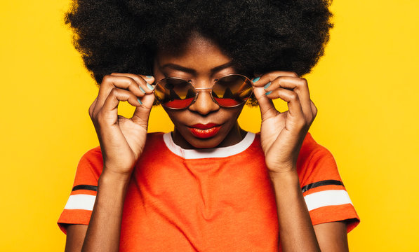 Beautiful Afro Woman posing over yellow background with round sunglasses