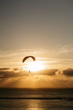 Silhouette of anonymous paraglider flying at sunset over the sea