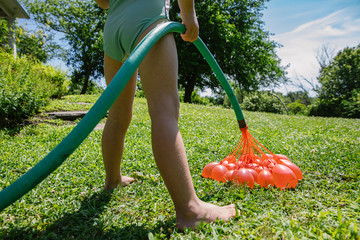 Young Girl with Hose Inflating Water Balloons in Backyard