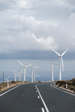 Wind turbines at two sides of highway road near ocean.