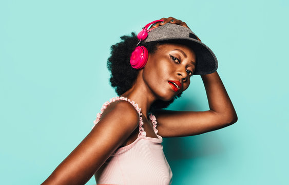 Beautiful Afro Woman posing over light blue background with pink headphones