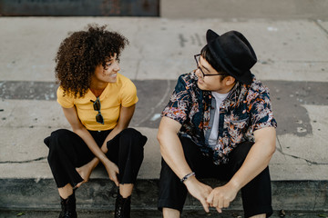 Two friends sitting on the sidewalk in the summer