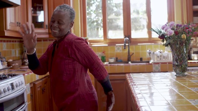 Smiling happy mature black woman dancing and celebrating life in her kitchen