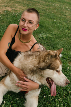 Short-haired girl with the malamut dog sit on the lawn at the park in the sun