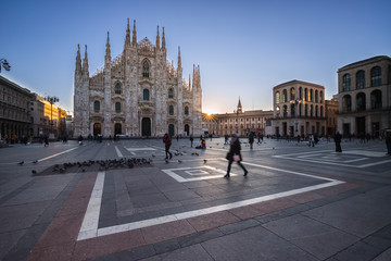 People cross the Piazza del Duomo in Milan during sunrise, Italy.