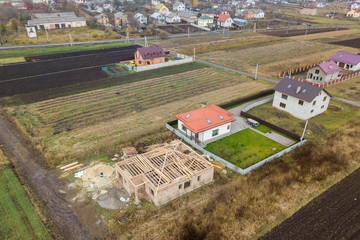 Top down aerial view of two private houses, one under construction with wooden roofing frame and...