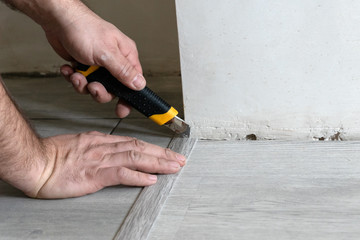worker's hand with cutter fits the laminate baseboard to the corner  during renovation process,...