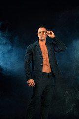 Portrait of handsome stylish man bodybuilder with naked torso in elegant suit. Guy in yellow sunglasses.