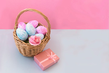 Fototapeta na wymiar Basket with Easter eggs on a delicate pink background, next to a pink box with a gift. Easter holiday concept