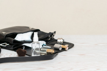 Close up of woman's black bag with antibacterial hand sanitizer, medical mask, napkins to prevent spread of bacteria. Personal hygiene concept to  avoid infections corona virus with copy space.