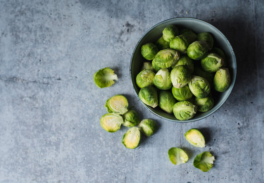 Overhead view of bowl of Brussels sprouts on cement counter.