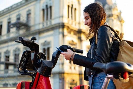 Woman taking a rental electric bike with her cell phone.