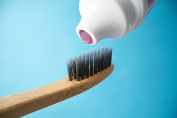 Pink toothpaste on a natural bamboo toothbrush with black charcoal bristles on a blue background