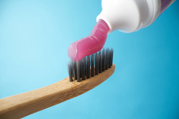 Pink toothpaste on a natural bamboo toothbrush with black charcoal bristles on a blue background