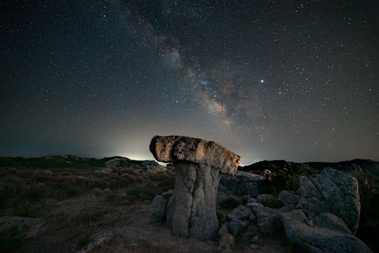 milky way panorama above a mushroom-shaped rock