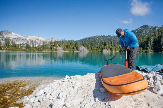 Adventurous man pumps up inflatable SUP next to a remote lake.