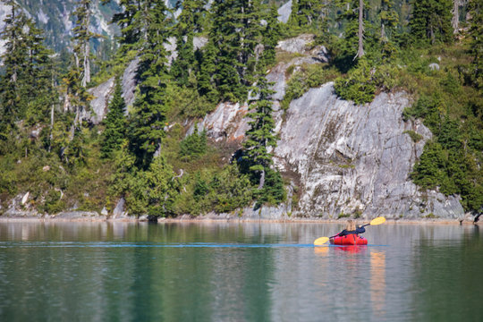 Rear view of retired woman paddling a packraft on remote lake.