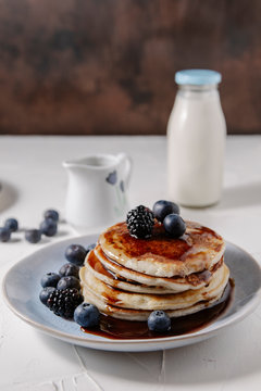 Pancakes topped with syrup and berries, with a bottle of milk in the background