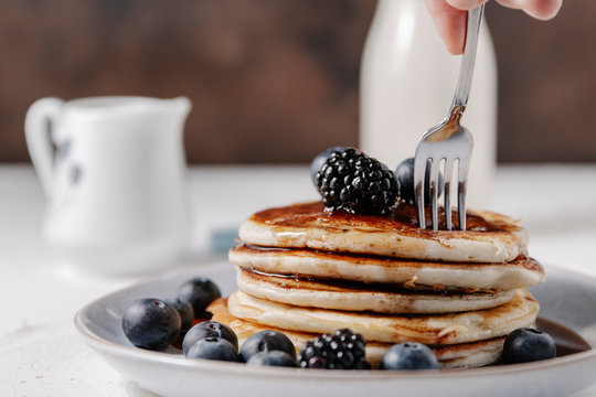Woman sticking a fork into a stack of homemade pancakes