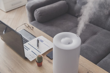 Household humidifier in the workplace to maintain relative humidity and microclimate in the workplace of the home office with a laptop and documents - obrazy, fototapety, plakaty