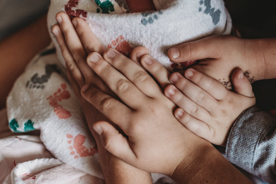 Close up detail of whole family's hands holding newborn son in hospita