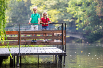 Two children boy and girl standing on wooden deck on a lake shore.