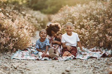 Four happy siblings sitting on blanket in flower field together