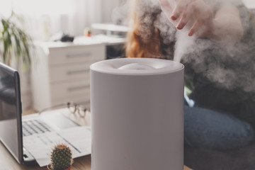 Woman freelancer uses a household humidifier in the workplace at home office with a laptop and documents. - obrazy, fototapety, plakaty