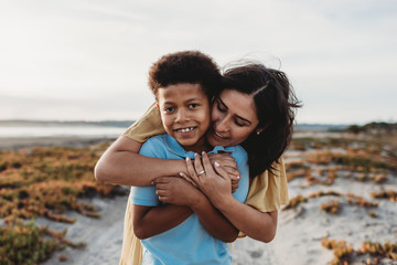 Front view close up portrait of young mother embracing son beach