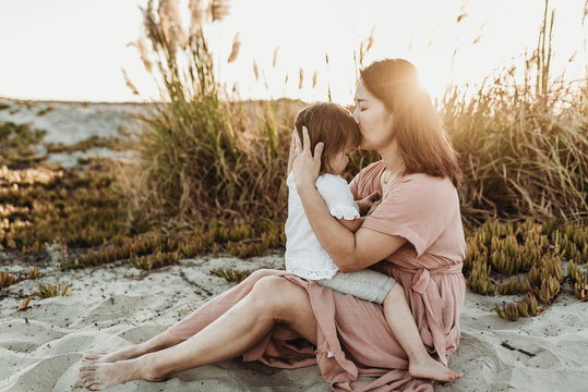 Side view of mother kissing young toddler at beach during sunset