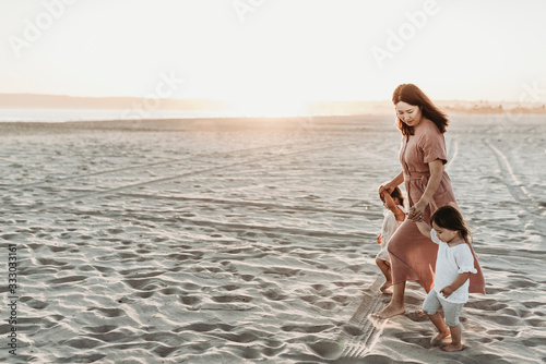 Side view of mother walking toddler twins to ocean with sun setting