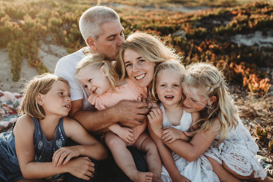 Lifestyle close up of family with young sisters sitting on beach